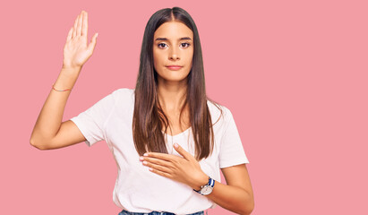 Young hispanic woman wearing casual white tshirt swearing with hand on chest and open palm, making a loyalty promise oath