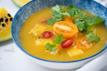 Close-up of yellow watermelon and tomatoes soup gazpacho served in a blue plate, selective focus