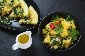 Salad with yellow watermelon cubes, herbed cucumber and fresh parsley, elevated view on a black stone background, studio shot