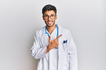 Young handsome man wearing doctor uniform and stethoscope cheerful with a smile of face pointing with hand and finger up to the side with happy and natural expression on face