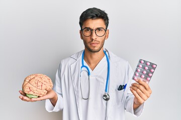 Young handsome man holding brain and pills as mental health concept skeptic and nervous, frowning...