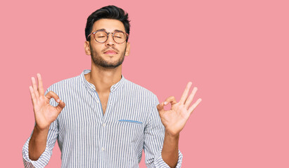 Young handsome man wearing casual clothes and glasses relax and smiling with eyes closed doing meditation gesture with fingers. yoga concept.