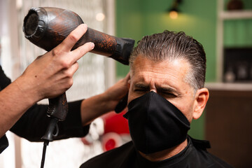 barber combs and blow-drives another man's hair in a barber shop during the coronavirus pandemic.