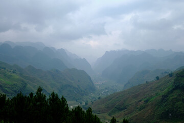 A winding mountain road winds through a valley lined by mountains gradually disappearing through the clouds in Duong Thuong in Ha Giang, northern Vietnam