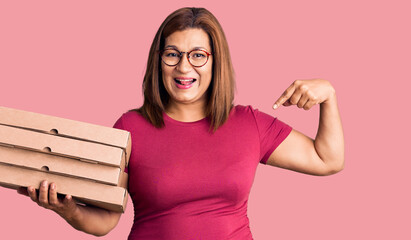 Middle age latin woman holding delivery pizza box pointing finger to one self smiling happy and...