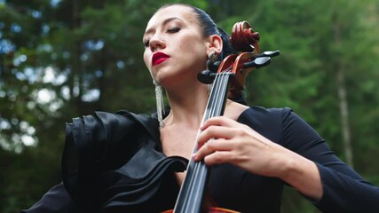 Passionate woman performs music. Attractive woman is playing the cello and enjoys the music by closing her eyes outdoors. Close-up.