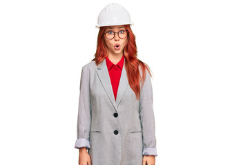 Young redhead woman wearing architect hardhat afraid and shocked with surprise expression, fear and excited face.