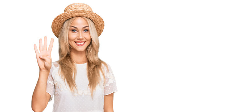 Young blonde girl wearing summer hat showing and pointing up with fingers number four while smiling confident and happy.