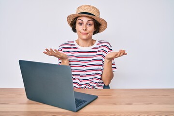 Young hispanic woman working with laptop sitting on the table clueless and confused expression with...