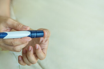 Close up of woman hands using lancet on finger to check blood sugar level by Glucose meter. Use as Medicine, diabetes, glycemia, health care and people concept.