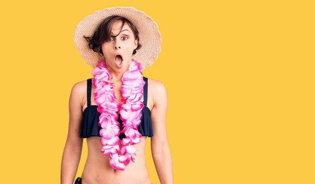 Beautiful young woman with short hair wearing bikini and hawaiian lei scared and amazed with open mouth for surprise, disbelief face