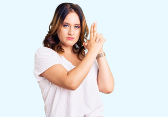 Young beautiful caucasian woman wearing casual white tshirt holding symbolic gun with hand gesture, playing killing shooting weapons, angry face