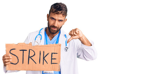Young hispanic man wearing doctor stethoscope holding strike banner with angry face, negative sign...