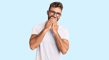 Young hispanic man wearing casual clothes and glasses laughing and embarrassed giggle covering...