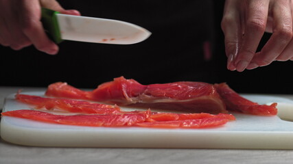 male chef cuts fillet of fresh salmon into large chunks. Cooking fish in kitchen. Preparation of...