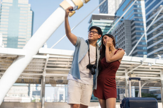 Asian tourist couple with suitcase selfie in city