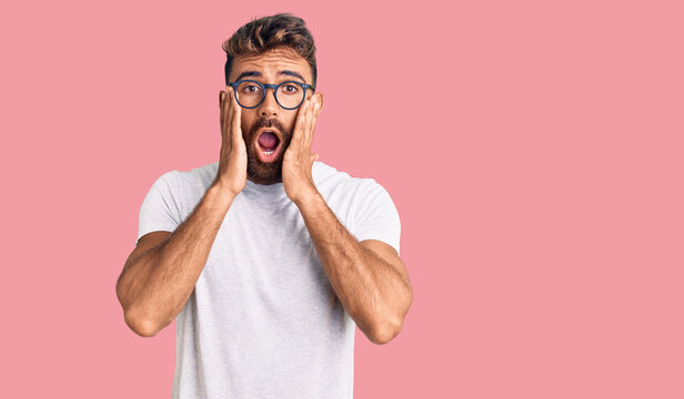 Young hispanic man wearing casual clothes and glasses afraid and shocked, surprise and amazed expression with hands on face