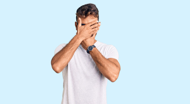Young hispanic man wearing casual clothes and glasses covering eyes and mouth with hands, surprised and shocked. hiding emotion