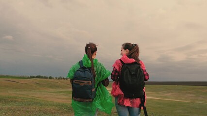 Healthy women tourists travel with backpacks in colorful raincoats. Slow motion. teamwork of travelers. Free girls-travelers go to edge of hill, rejoice, clap their hands and jump with happiness.