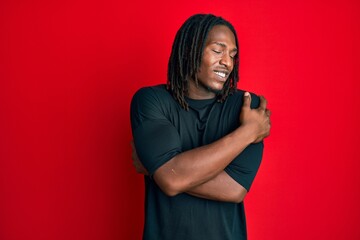 African american man with braids wearing casual clothes hugging oneself happy and positive, smiling...