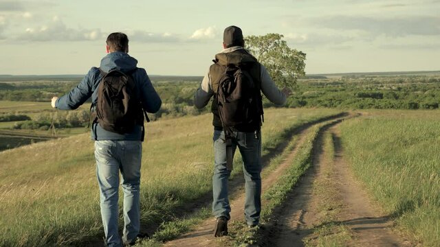 Travelers with backpacks are walking along the road. Teamwork. Adventure and travel concept. Tourists enjoy relaxation and nature.