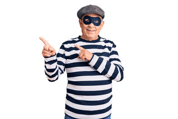 Senior handsome man wearing burglar mask and t-shirt smiling and looking at the camera pointing with two hands and fingers to the side.