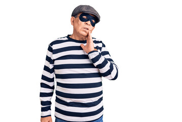 Senior handsome man wearing burglar mask and t-shirt touching mouth with hand with painful expression because of toothache or dental illness on teeth. dentist