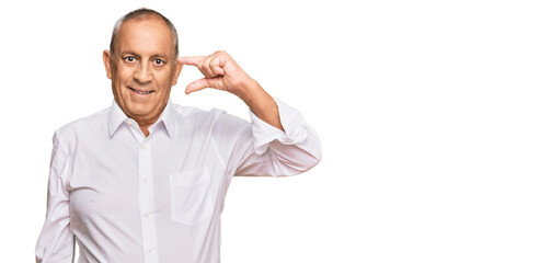 Handsome senior man wearing elegant white shirt smiling and confident gesturing with hand doing small size sign with fingers looking and the camera. measure concept.