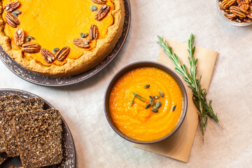 Autumn party, pumpkin dinner: orange soup, pumpkin pie decorated with pecans on a served table and other dishes