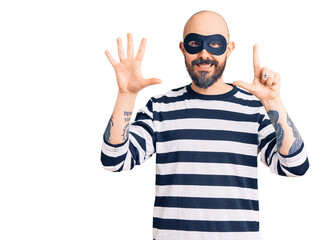 Naklejka premium Young handsome man wearing burglar mask showing and pointing up with fingers number seven while smiling confident and happy.