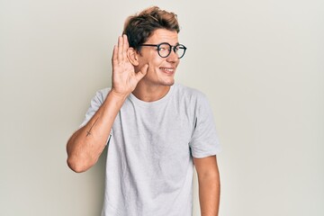 Fototapeta na wymiar Handsome caucasian man wearing casual clothes and glasses smiling with hand over ear listening and hearing to rumor or gossip. deafness concept.
