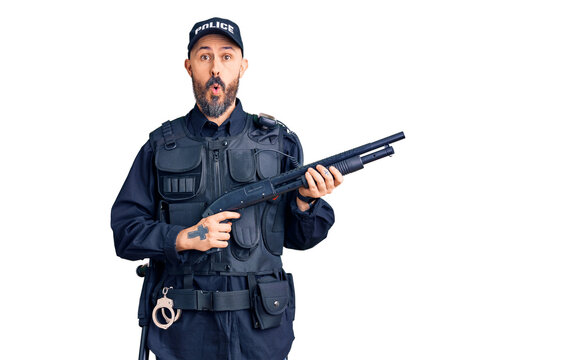 Young handsome man wearing police uniform holding shotgun scared and amazed with open mouth for surprise, disbelief face