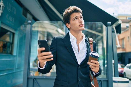 Young caucasian businessman with serious expression using smartphone and drinking coffee at the city.