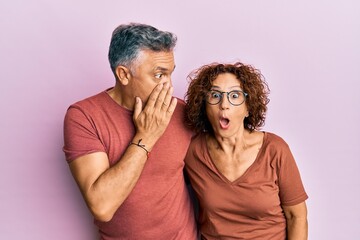 Beautiful middle age couple together wearing casual clothes hand on mouth telling secret rumor,...