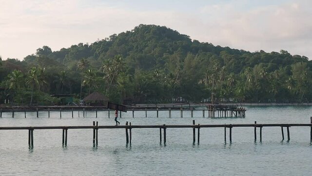 workers walking on wooden bridge over the sea near tropical beach resort. sunrise in the morning with beam on mountain.