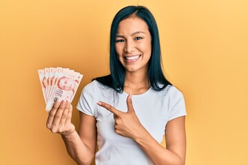 Beautiful hispanic woman holding 10 singapore dollars banknotes smiling happy pointing with hand and finger