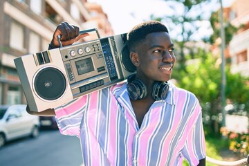 Young african american man listening to music using boom box and headphones walking at street of city. © Krakenimages.com