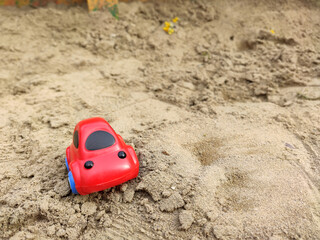 Fototapeta na wymiar a child left a red toy car on the sand on a children's Playground