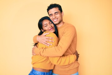 Beautiful latin young couple wearing casual clothes together hugging oneself happy and positive,...