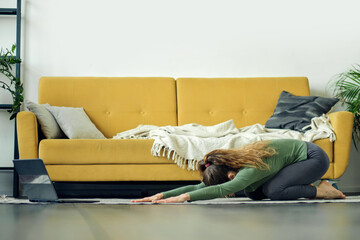 Beautiful young woman doing yoga at home. Fitness training online.