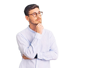 Handsome young man with bear wearing elegant business shirt and glasses with hand on chin thinking about question, pensive expression. smiling with thoughtful face. doubt concept.