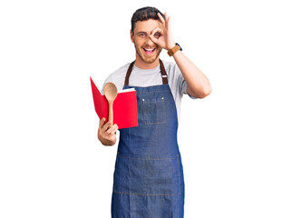 Handsome young man with bear wearing professional baker apron reading cooking recipe book smiling happy doing ok sign with hand on eye looking through fingers