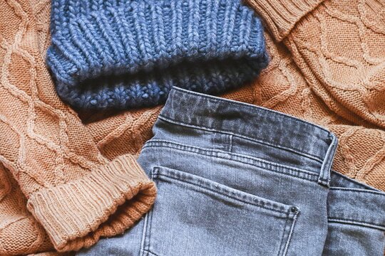 Blue woolen hat, brown knitted sweater and gray jeans. Fall and winter fashion outfit. Autumn clothes essentials