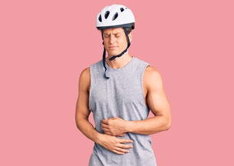Young handsome man wearing bike helmet with hand on stomach because indigestion, painful illness feeling unwell. ache concept.