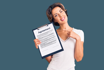 Young beautiful woman holding clipboard with agreement document smiling happy pointing with hand and finger