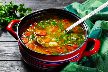 Pea soup with sausage and parsnip in red saucepan