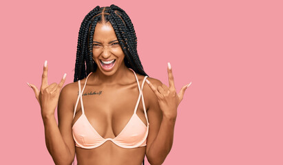 Beautiful hispanic woman wearing bikini shouting with crazy expression doing rock symbol with hands...