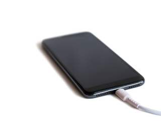 black smartphone with connected cable for charging the battery on white background