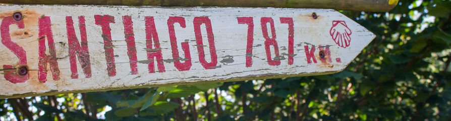 Spain - 10/11/2019: Camino de Santiago sign. Wooden board with distance to Santiago de Compostela. Pilgrimage concept. Religious road marker. Pilgrimage symbol in forest. Travel destinations concept.