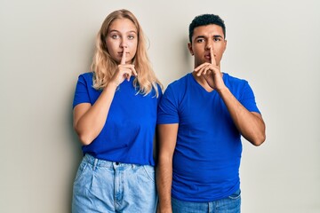 Young interracial couple wearing casual clothes asking to be quiet with finger on lips. silence and secret concept.